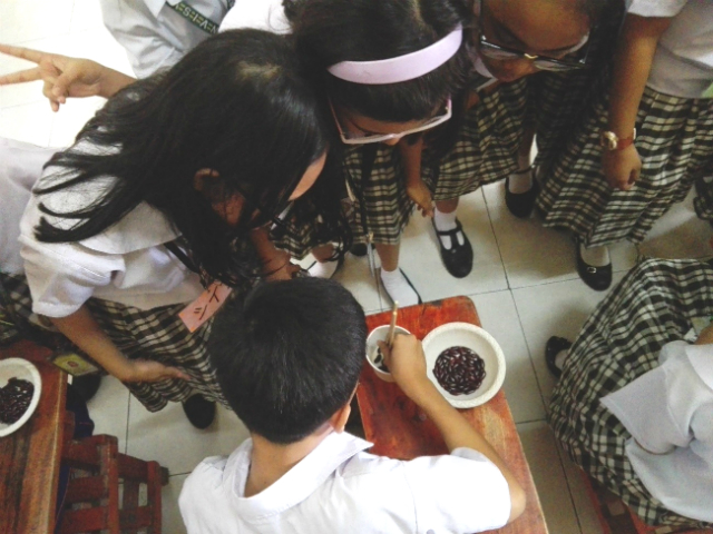豆つかみの器をのぞき込む生徒たちの写真