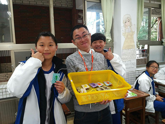 折り紙のポチ袋を持った山本さんと生徒たちの写真