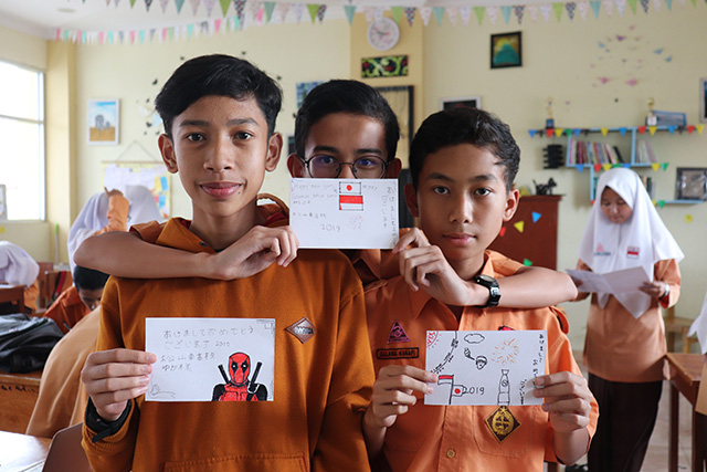 日本とインドネシアの国旗が描かれた年賀状を持つ生徒の写真