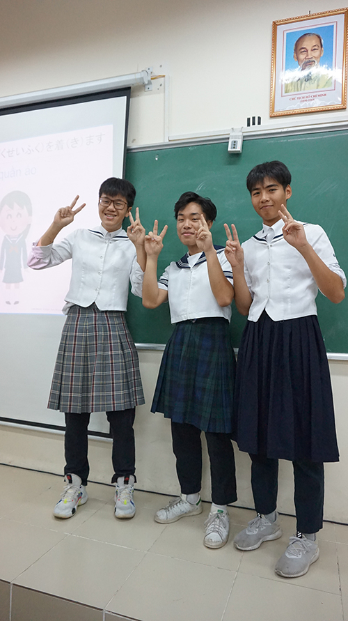セーラー服を着た男子生徒と、後ろに笑顔を浮かべたホーチミンの写真が飾られた写真